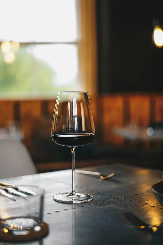 A glass of red wine on a zinc table by a window.
