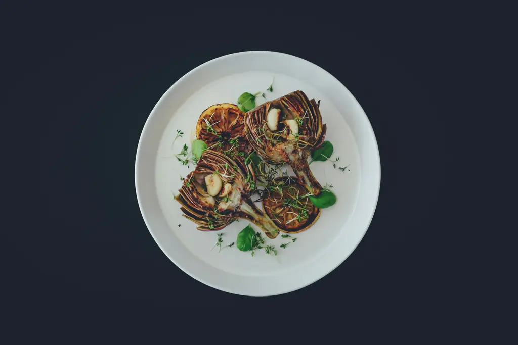 Roasted, halved vegetables with herbs on a white plate, on a dark slate background.
