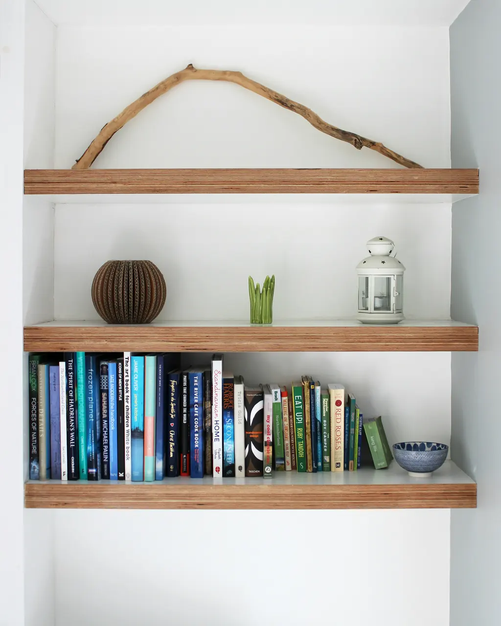 Three oak shelves fitted into a white-painted alcove, with books and a branch on them.