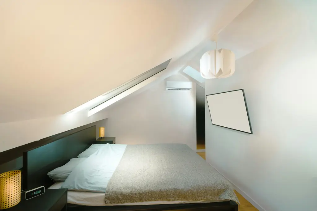 A bed under a sloping ceiling in a small, dim attic room.