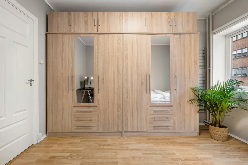 A wall of fitted oak wardrobes with two mirrored doors in a bright bedroom.