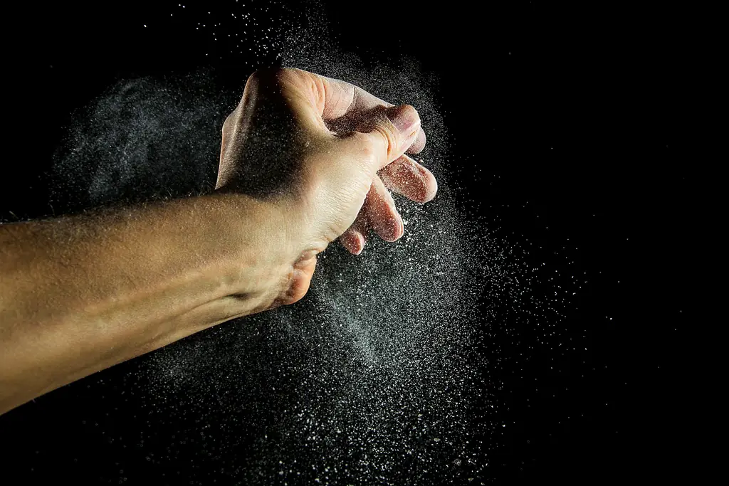 A hand clapping out a cloud of white lifting chalk against a black background.