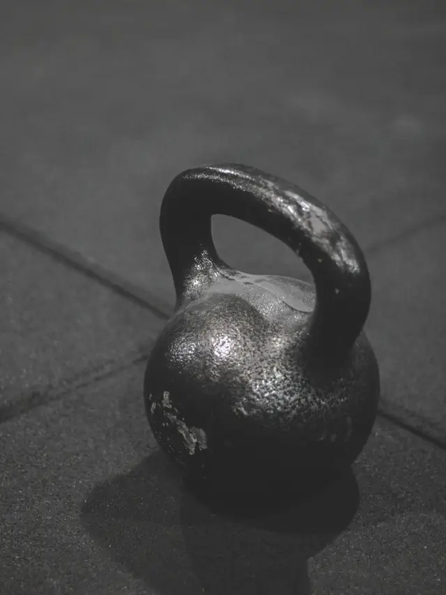 A black kettlebell on a rubber gym floor, in black and white.