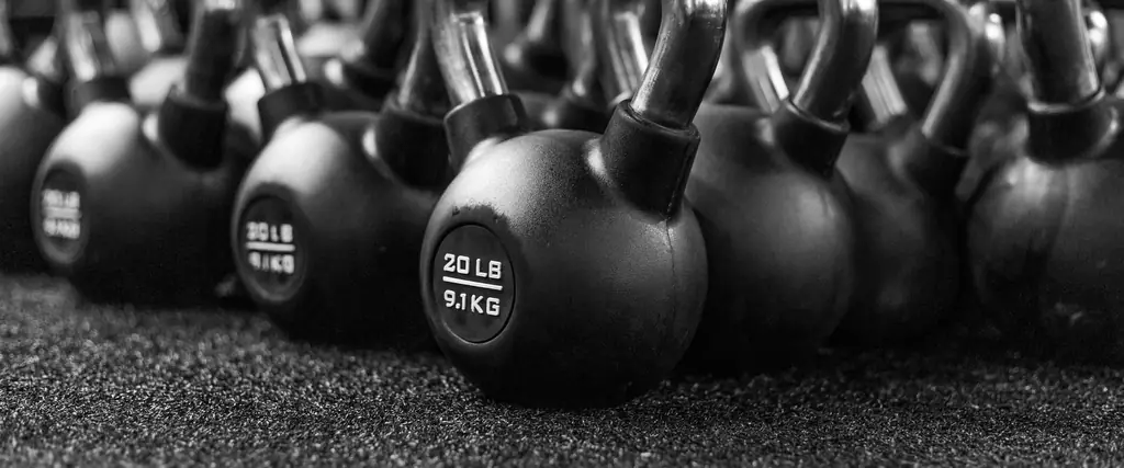 Rows of black kettlebells lined up on a gym floor, in black and white.