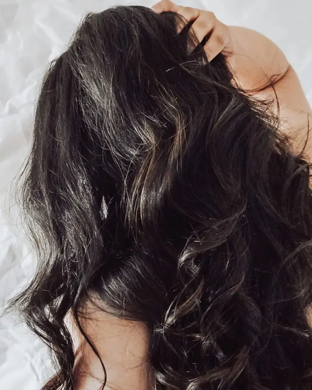 Long, glossy dark waves seen from behind against a pale crumpled sheet.