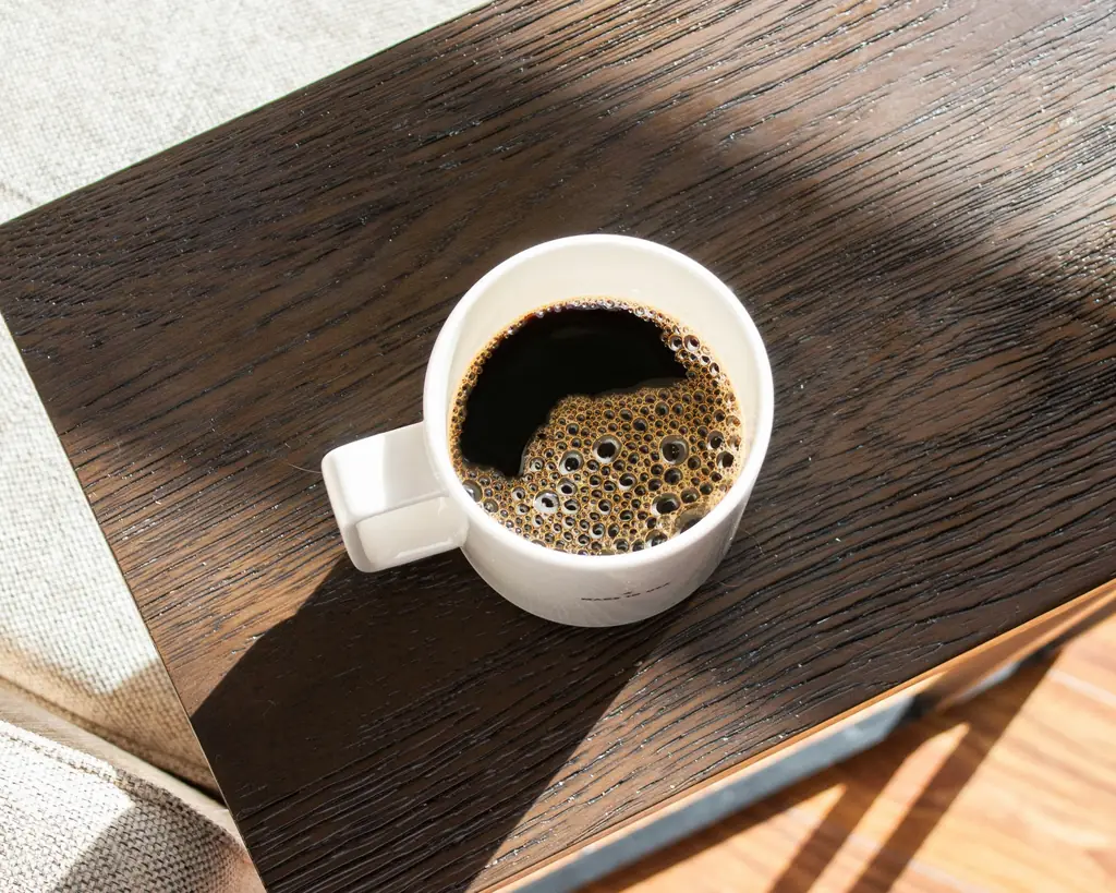 A white mug of black filter coffee on a dark wooden table, in a stripe of morning sun.
