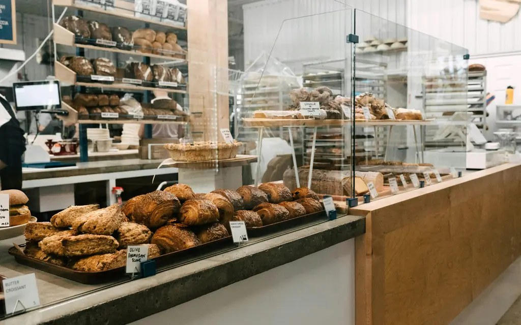 A bakery counter lined with loaves and pastries under glass, with shelves of bread behind it.