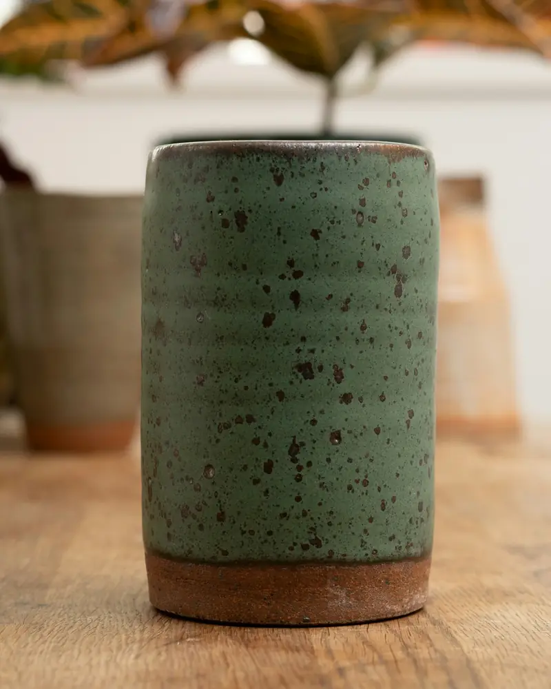 A tall speckled tumbler in a deep moss-green glaze, its base left as bare clay.