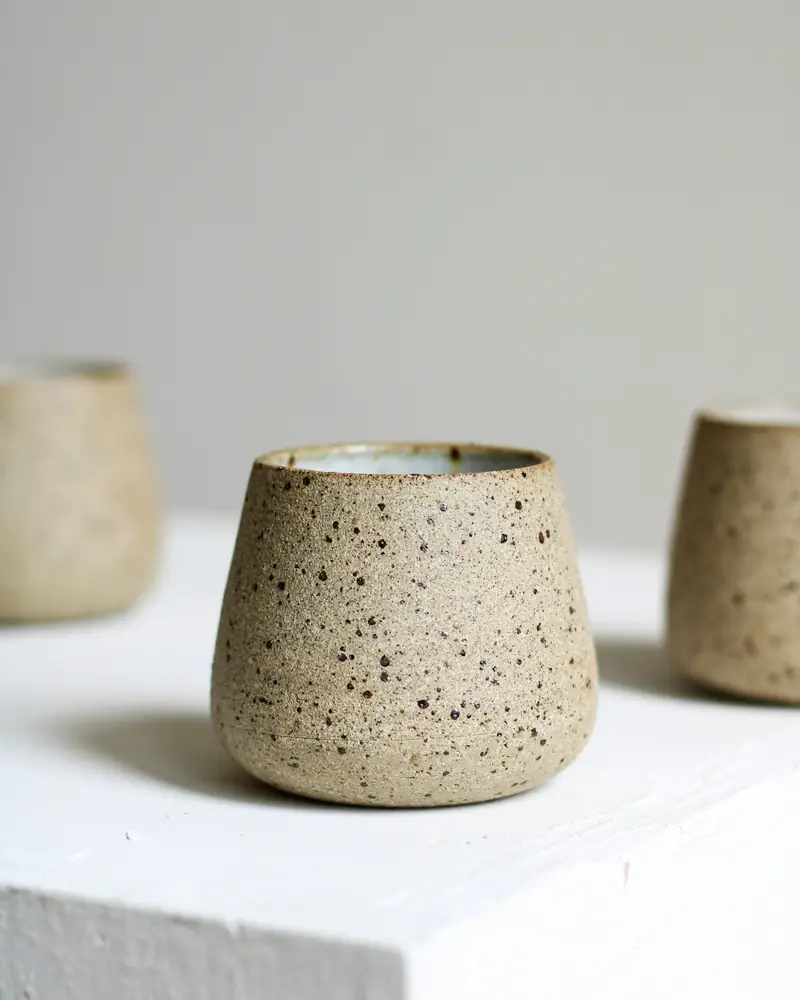 A speckled oatmeal stoneware cup on a white plinth.