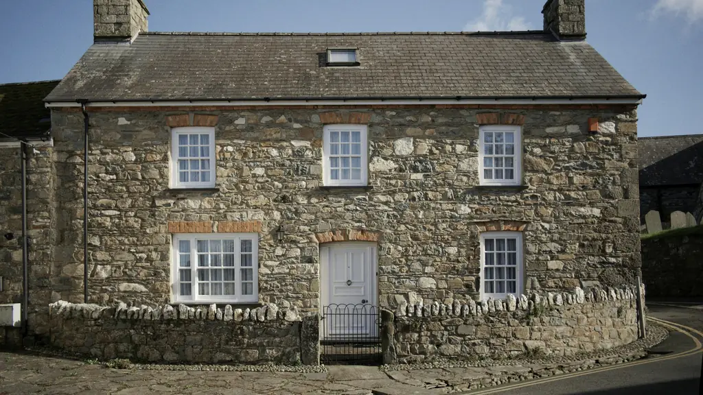 A two-storey stone cottage with white sash windows, a white front door and a low stone wall, under a blue sky.