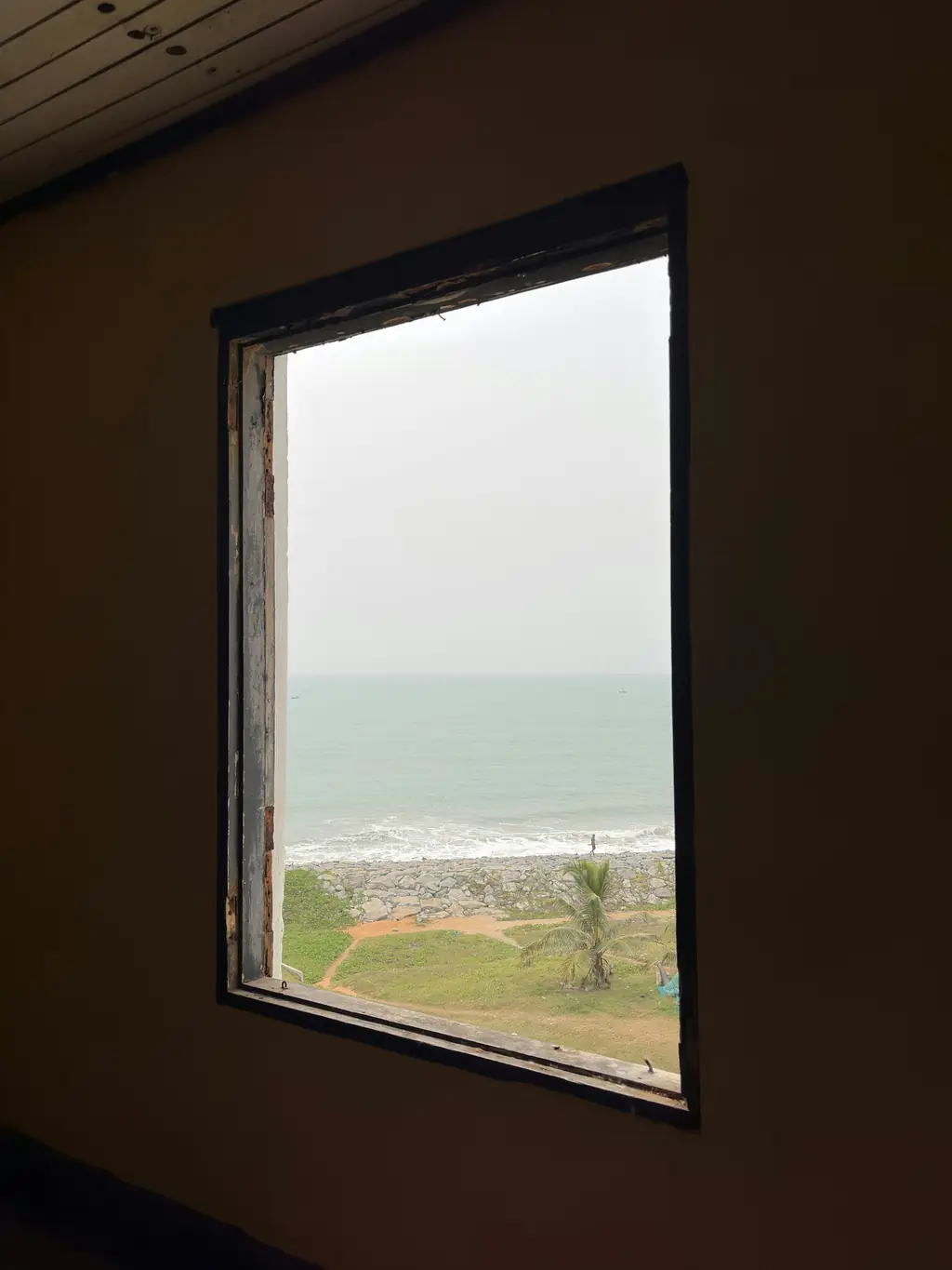 The sea through an open window in a dark room: a grey horizon, a strip of beach and the edge of a green.