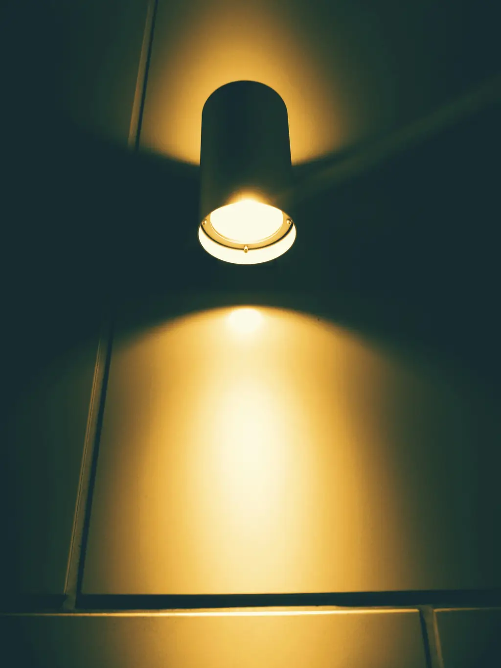A ceiling downlight casting a warm pool of light down a dark green wall.