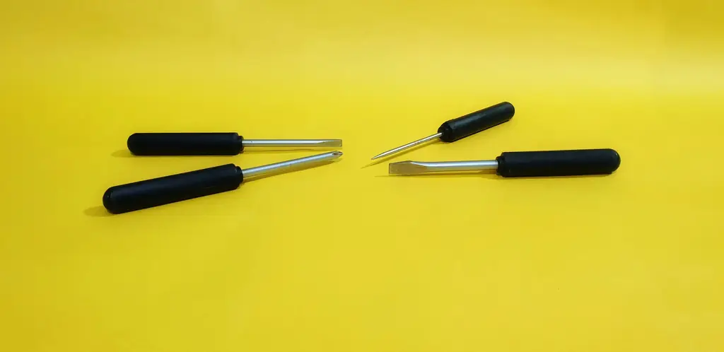 Four black-handled screwdrivers laid out on a bright yellow surface.