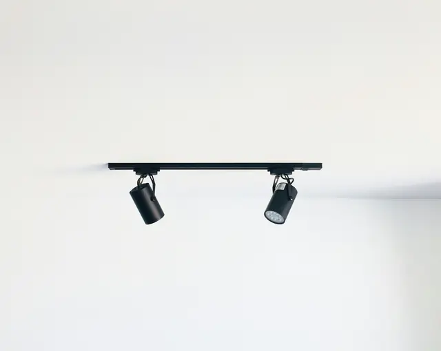 Two black spotlights on a short ceiling track against a white wall.