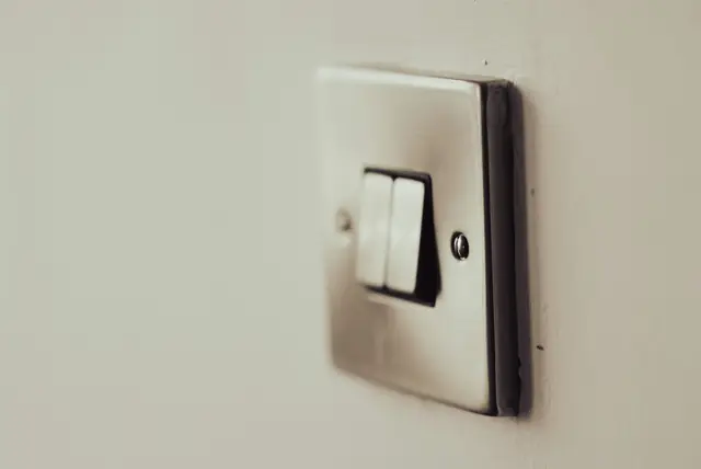 A brushed steel double light switch on a white wall, seen at an angle.