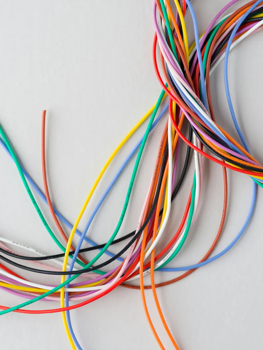 A loose bundle of coloured electrical wires, red, orange, green, blue and yellow, on a pale background.
